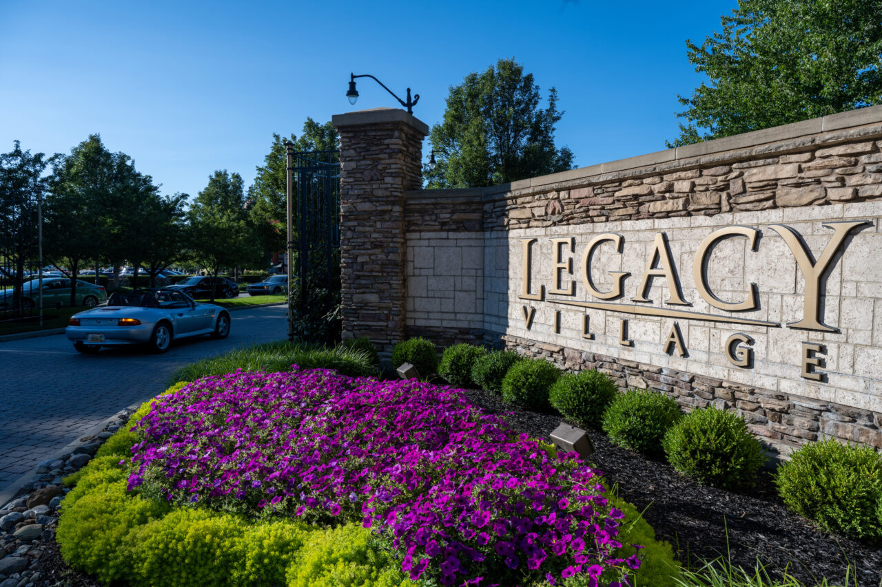 An outdoor sign at Legacy Village with a garden below